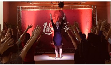 Laura Poltosi em palestra com plateia participando de mãos levantadas.